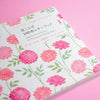 A stack of floral writing and drawing papers on a solid pink background. The papers feature a white base with a repeating pattern of pink flowers and green leaves, with Japanese and English text on the top sheet reading 'Beautiful Floral Papers' and '100 Writing and Crafting Papers'.