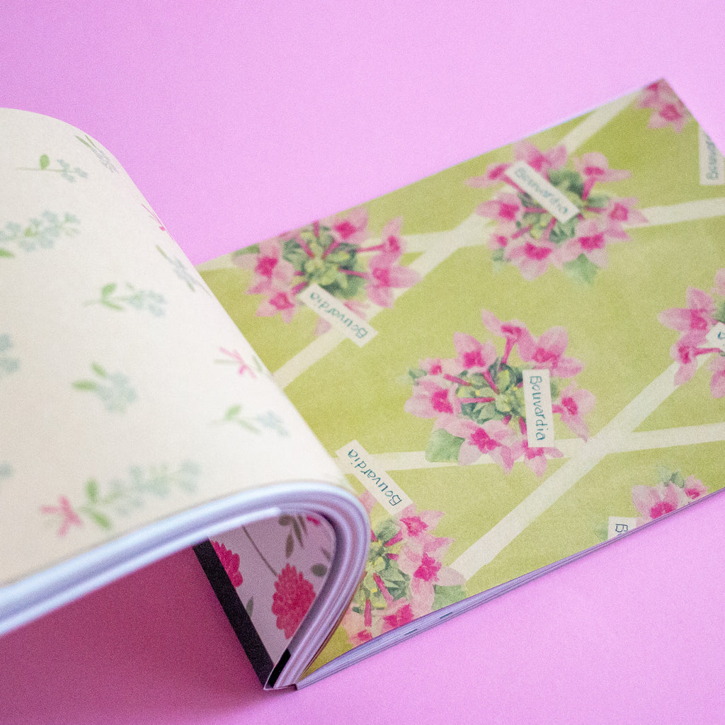 An open notebook on a solid pink background, showing floral patterned pages.