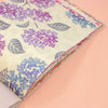A close-up of a book or notebook with a cream-coloured page decorated with purple and blue floral patterns, resting on a soft peach-pink background.