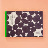 A Japanese paper notebook with a black and white organic patterned cover and a bright green spine, displayed on a peach-coloured background.
