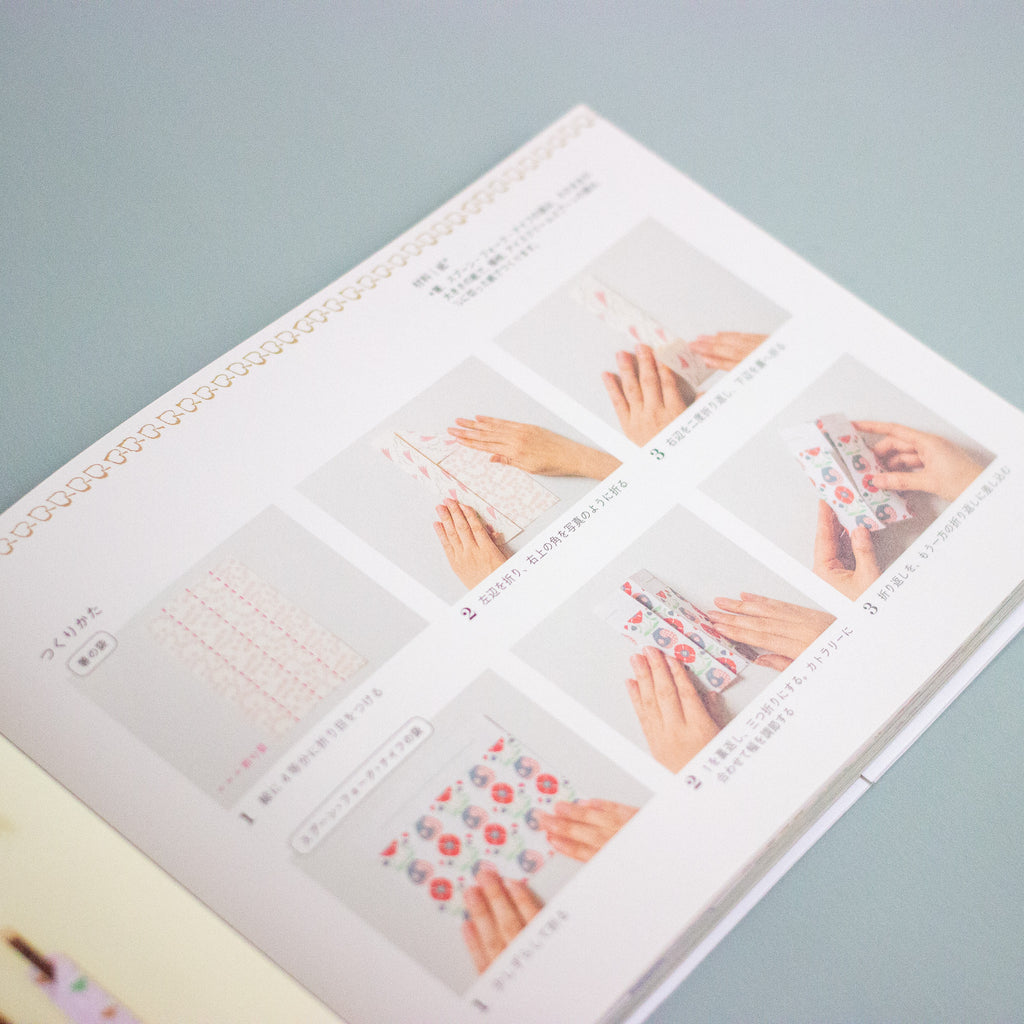 An open booklet or instruction manual showing printed steps for wrapping a phone with decorative paper, photographed on a pale blue background.