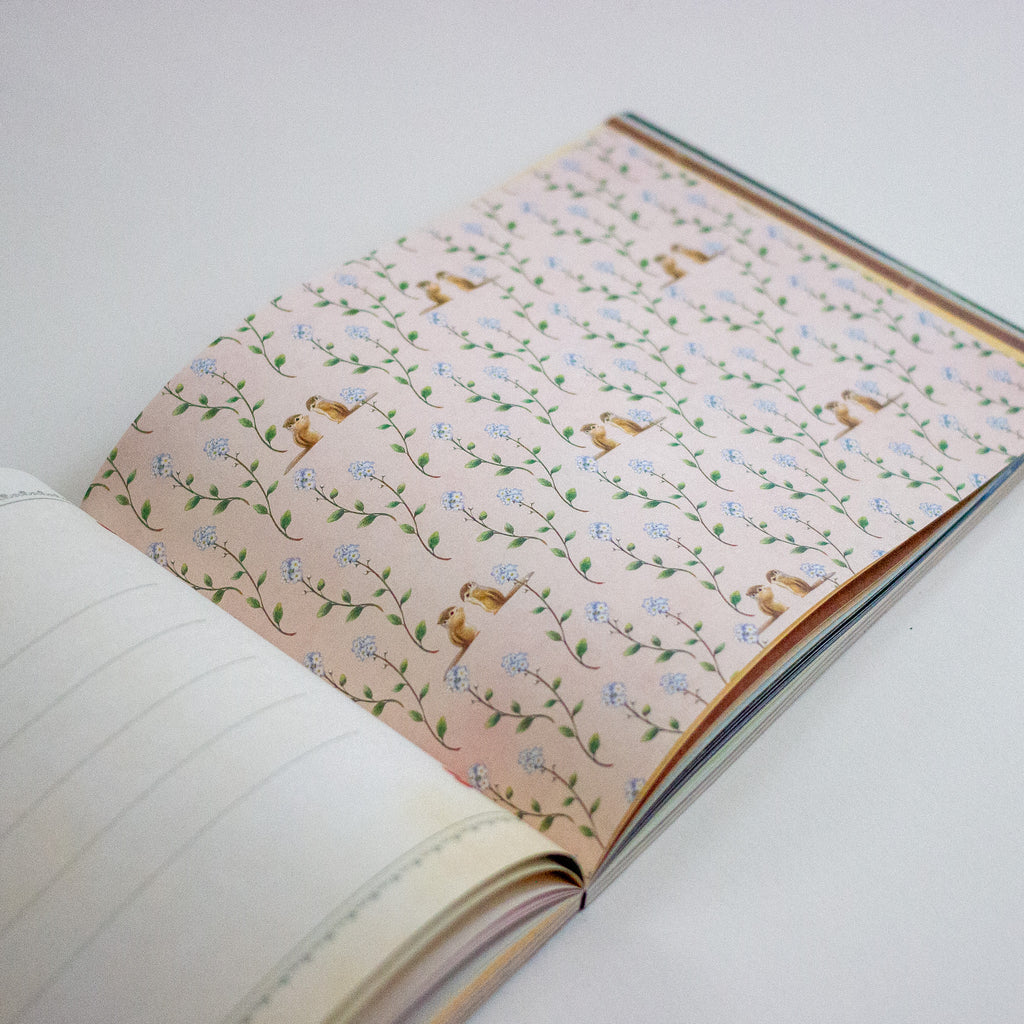 Open notebook with decorative floral and squirrel patterned endpapers on a white background