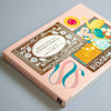 A book titled 'The Sweets of A La Car-Do 100 Writing & Crafting Papers' with a light pink cover, featuring decorative illustrations and Japanese text on the front, photographed on a neutral grey background.
