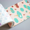 A notebook or journal shown open at an angle, with the right page featuring a pastel pattern of ice cream cones, candy canes, and sweets on a pale pink background. The left page has a light blue and white geometric pattern.