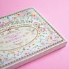 A decorative book cover with floral and butterfly illustrations, photographed on a solid pink background.