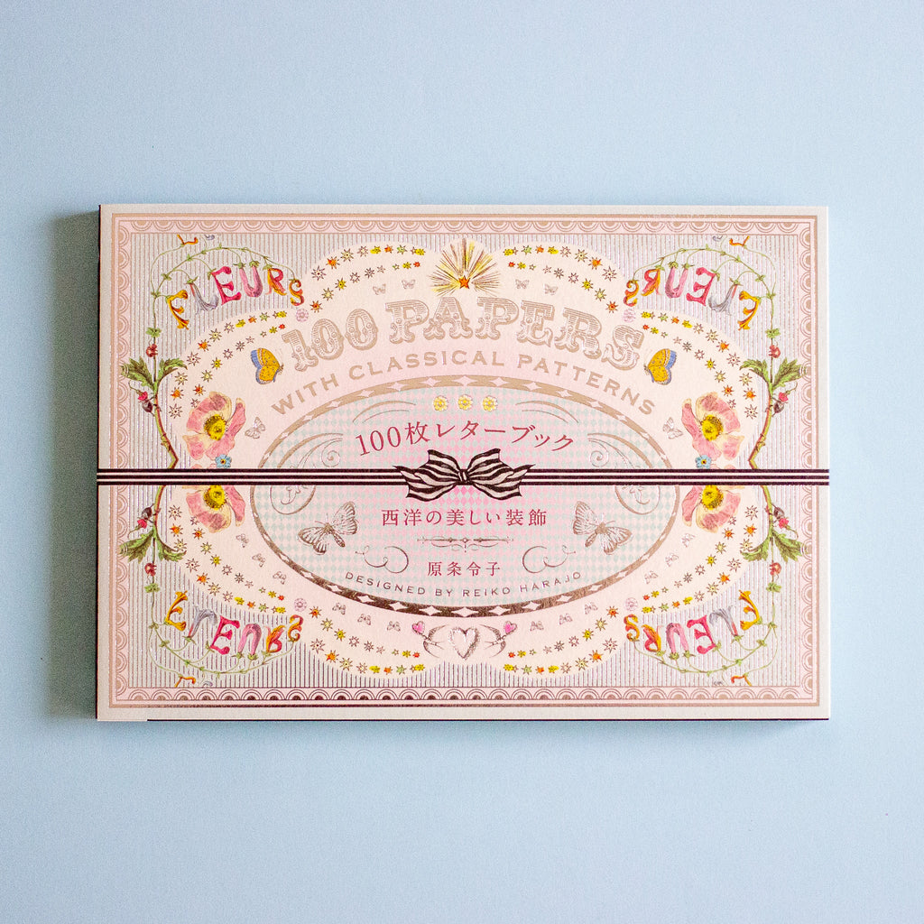 A decorative paper pack box with ornate vintage-style floral and scroll artwork in soft pink, beige, yellow, and green tones, wrapped with a dark ribbon across the center. The box reads '100 PAPERS' and 'WITH CLASSICAL PATTERNS' in English, with additional Japanese text.