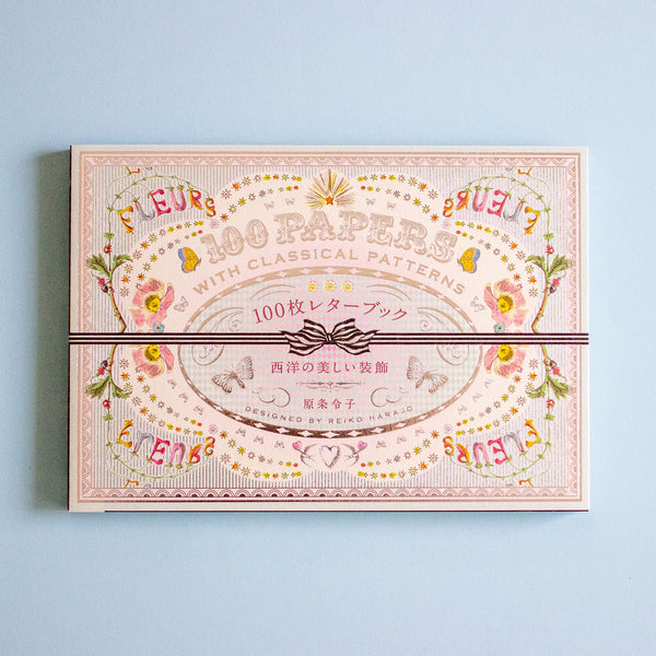 A decorative paper pack box with ornate vintage-style floral and scroll artwork in soft pink, beige, yellow, and green tones, wrapped with a dark ribbon across the center. The box reads '100 PAPERS' and 'WITH CLASSICAL PATTERNS' in English, with additional Japanese text.