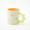 White mug with floral designs and a yellow handle on a white background