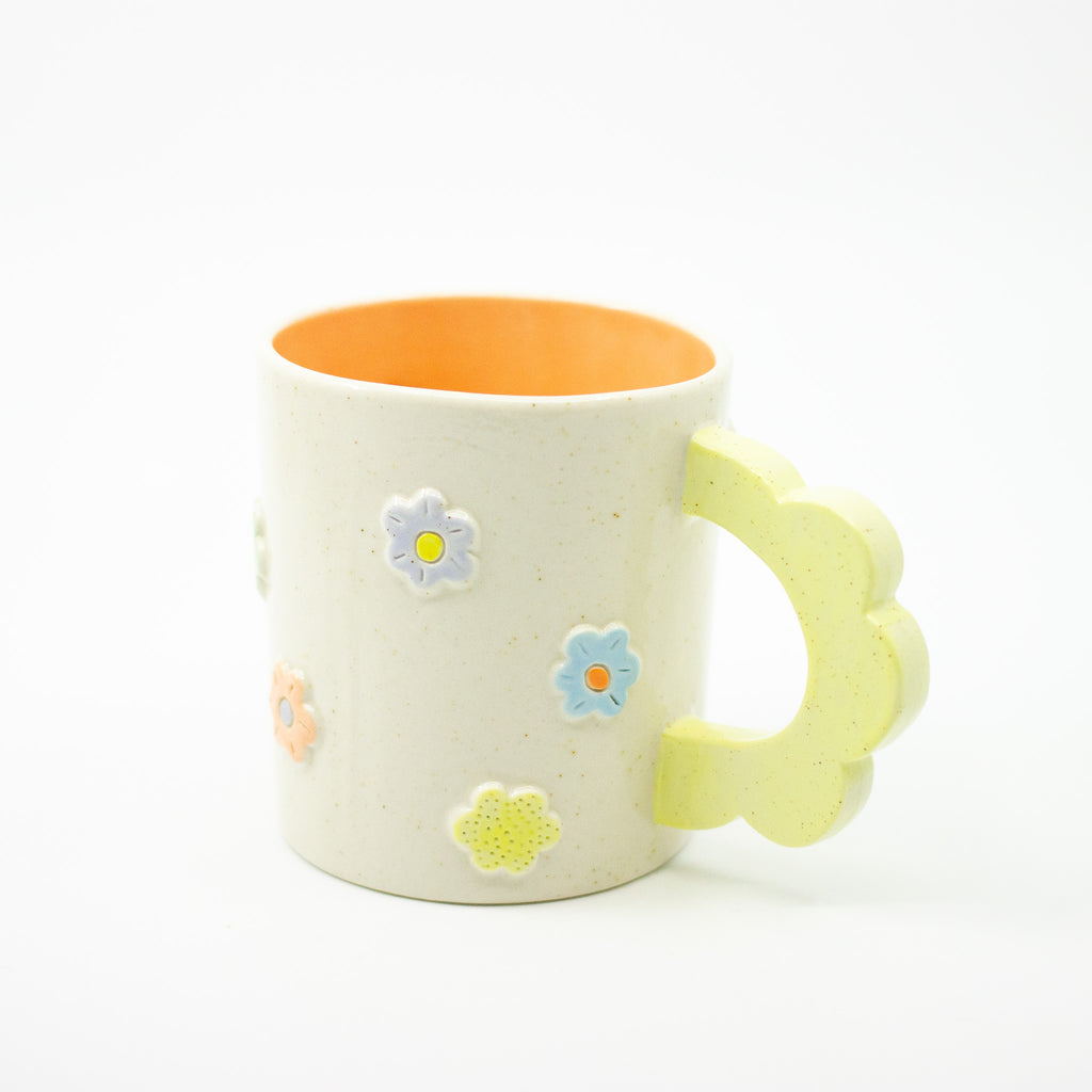 White mug with floral designs and a yellow handle on a white background