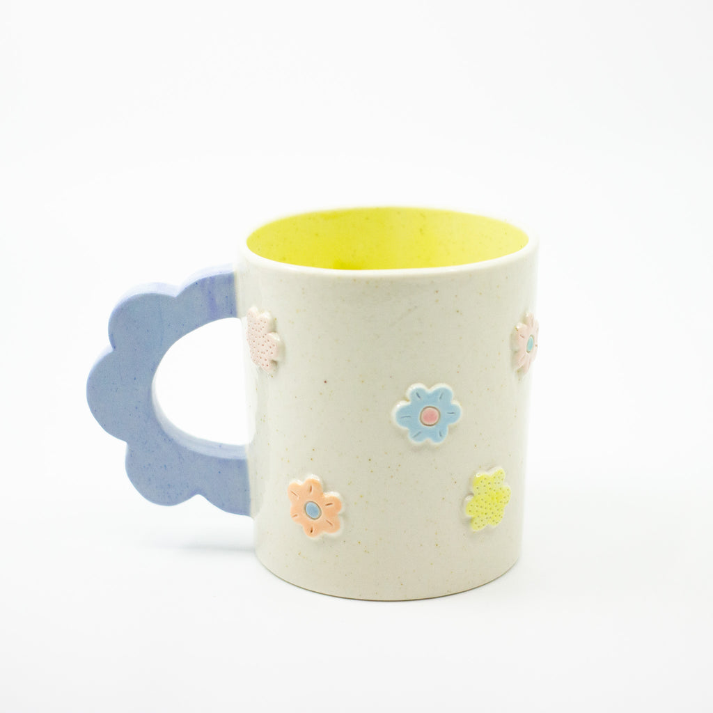 Ceramic mug with floral decorations and blue handle on a white background