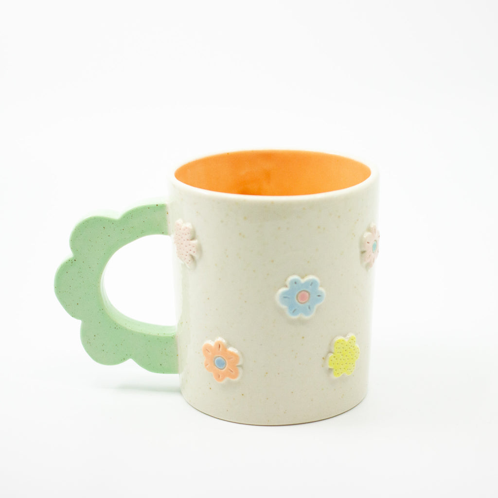 Ceramic mug with floral designs and mint green handle on a white background
