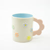 Ceramic mug with floral designs a pink handle, and a light blue interior on a white background
