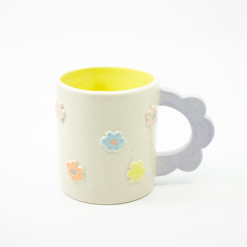 White mug with colorful flower designs and a violet handle on a white background