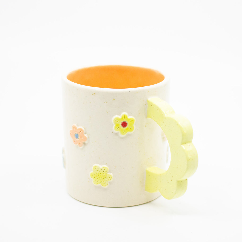 Closeup photo of the citrus 3D flower mug. Mug has light glaze with orange interior glaze. Flower shaped handle is citrus coloured. Mug has raised 3D style flowers that are hand painted and glazed in different colours. 