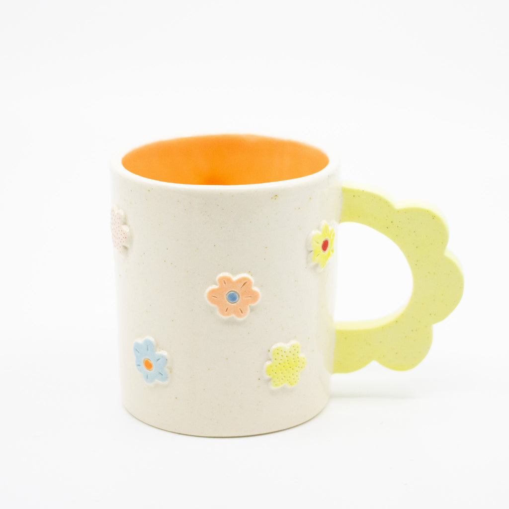 Closeup photo of the citrus 3D flower mug. Mug has light glaze with orange interior glaze. Flower shaped handle is citrus coloured. Mug has raised 3D style flowers that are hand painted and glazed in different colours. 