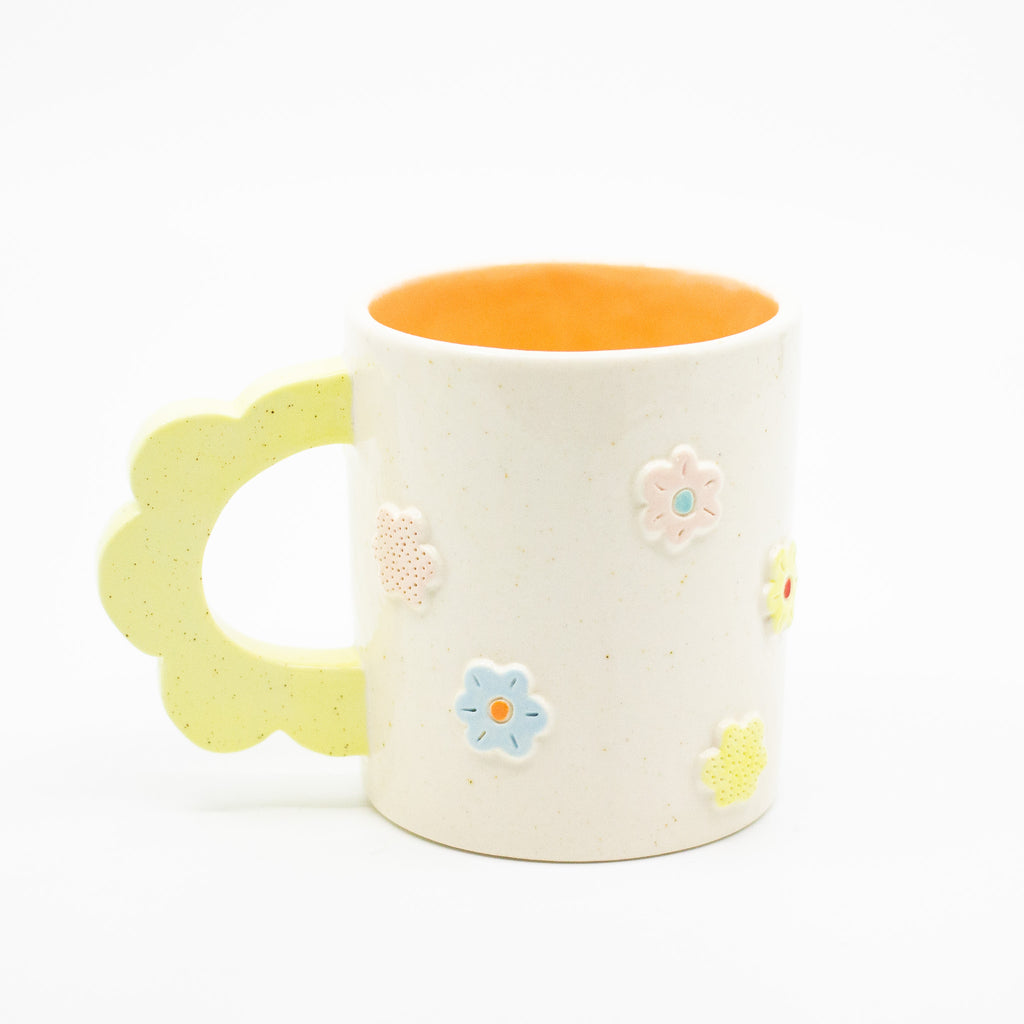 Closeup photo of the citrus 3D flower mug. Mug has light glaze with orange interior glaze. Flower shaped handle is citrus coloured. Mug has raised 3D style flowers that are hand painted and glazed in different colours. 