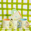 Set of four colorful mugs with floral designs on a green checkered background