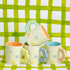 Set of four colorful ceramic mugs with floral designs on a green checkered background