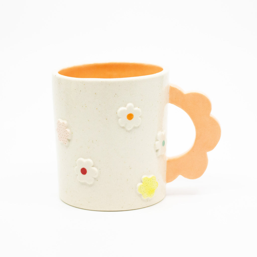 Closeup photo of the Peach 3D flower mug. Mug has light glaze with orange interior glaze. Flower shaped handle is peach coloured. Mug has raised 3D style flowers that are hand painted and glazed in different colours. 