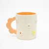 Closeup photo of the Peach 3D flower mug. Mug has light glaze with orange interior glaze. Flower shaped handle is peach coloured. Mug has raised 3D style flowers that are hand painted and glazed in different colours. 