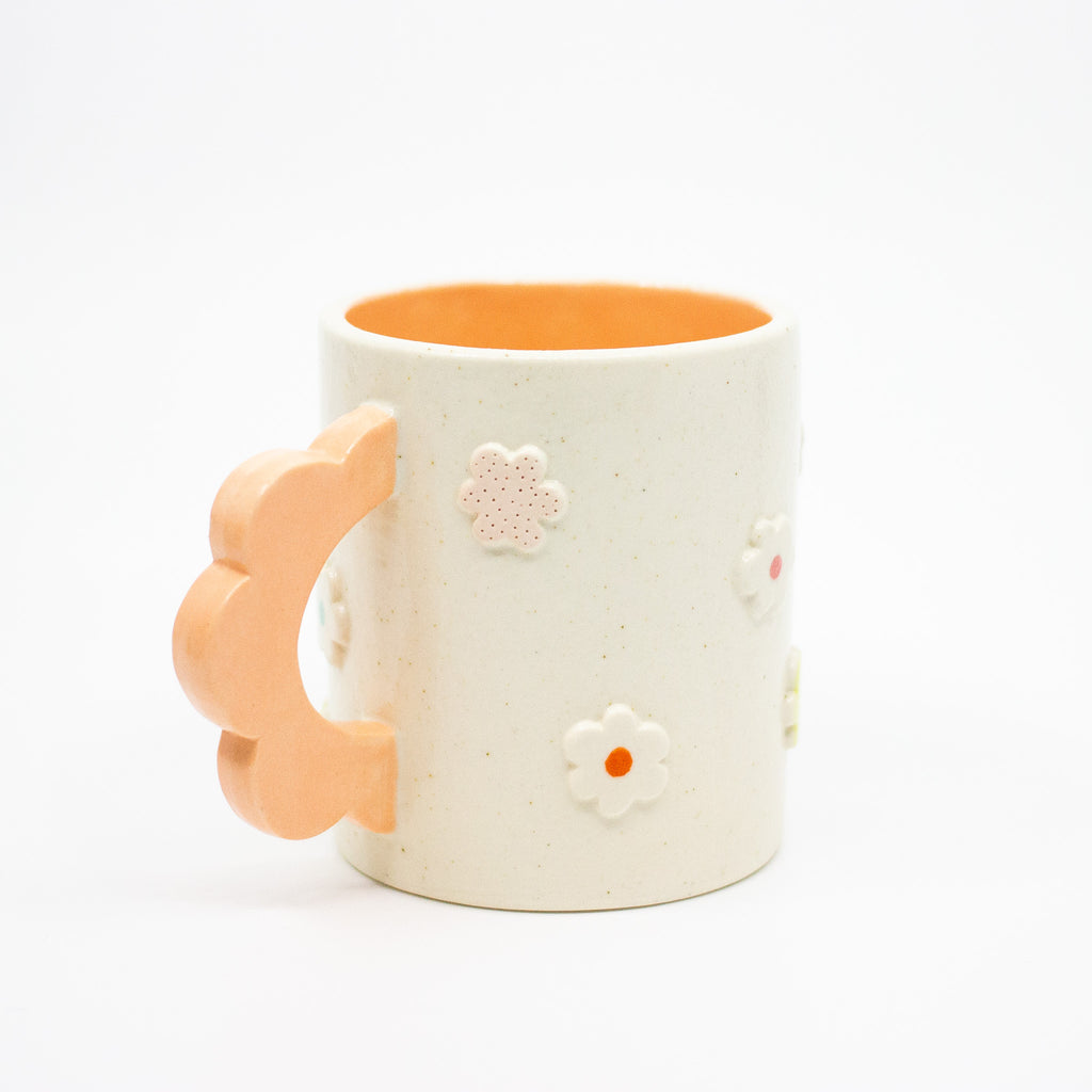 Closeup view of the Peach 3D flower mug handle. Mug has light glaze with orange interior glaze. Flower shaped handle is peach coloured. Mug has raised 3D style flowers that are hand painted and glazed in different colours. 