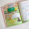 Open children's book with illustrations of animals and a trash truck on a white surface