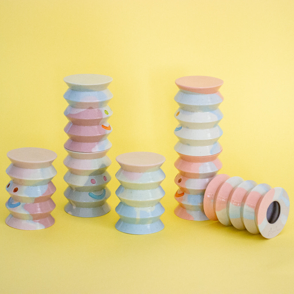 Stacked pastel-coloured cylindrical ceramic objects on a yellow background