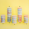 Stacked pastel-coloured cylindrical ceramic objects on a yellow background