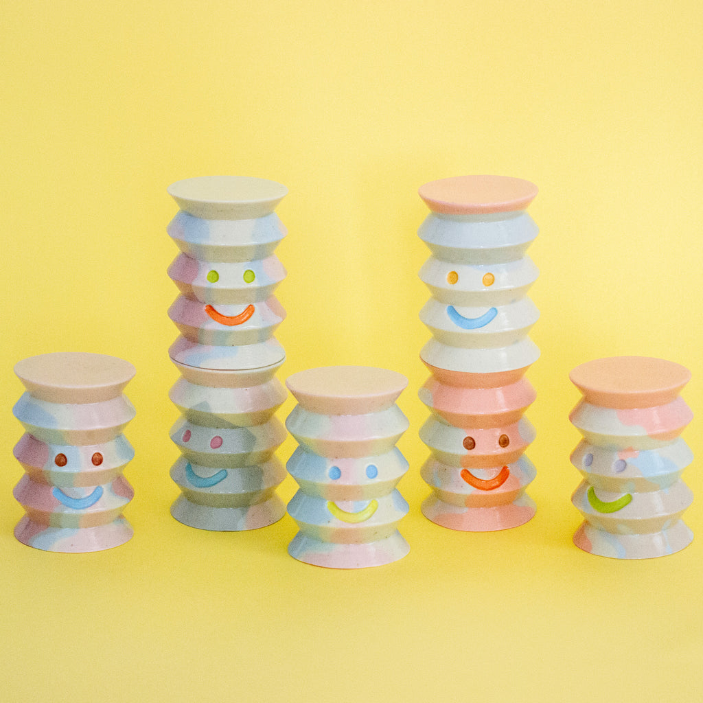Stacked pastel-coloured cylindrical ceramic figurines on a yellow background