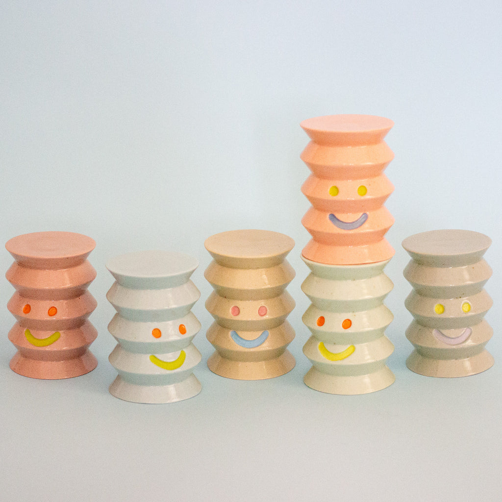 Set of colorful stacked ceramic figurines with smiley face designs on a light gray background
