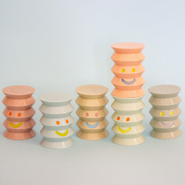 Set of colorful stacked ceramic figurines with smiley face designs on a light gray background
