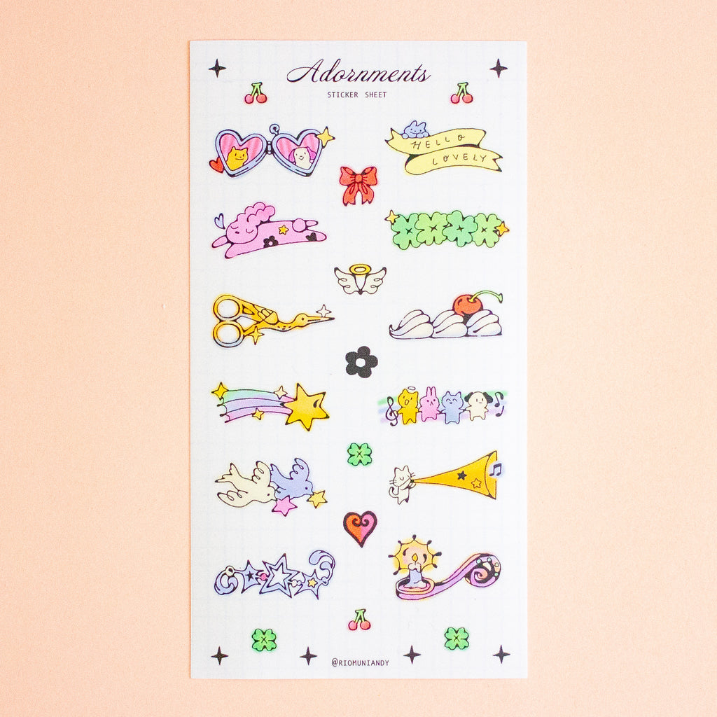 A sticker sheet featuring cute pastel-coluored cartoon illustrations, including cherries, hearts, bows, a green flower, scissors, a rainbow, stars, and small characters, displayed on a soft peach background.