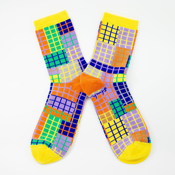 Colourful grid-patterned socks with yellow cuffs and toes, orange heels, and multicoloured squares in purple, green, blue, and orange. Designed by shuh. and made in Australia.