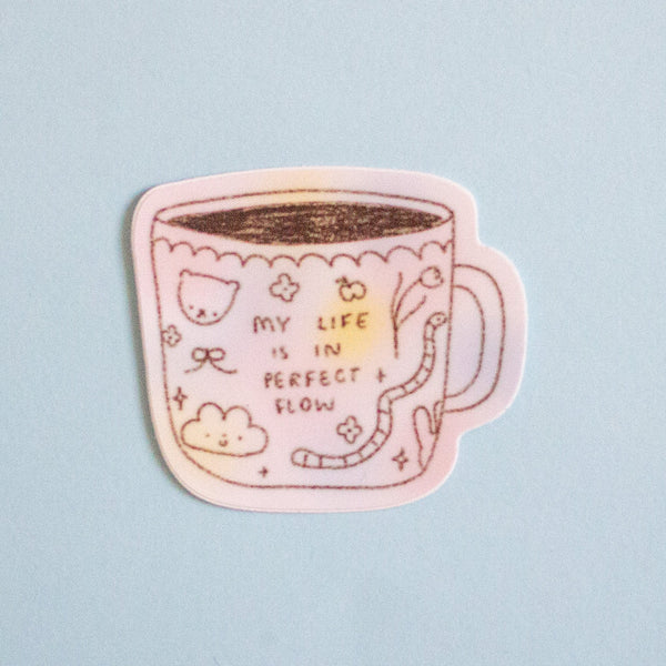A die-cut sticker featuring a cute pink coffee mug illustration with the text 'MY LIFE IS IN PERFECT SLOW' and small doodles, shown on a light blue background.