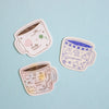 Three cute illustrated coffee mugs with pastel designs and text, arranged on a light blue background.