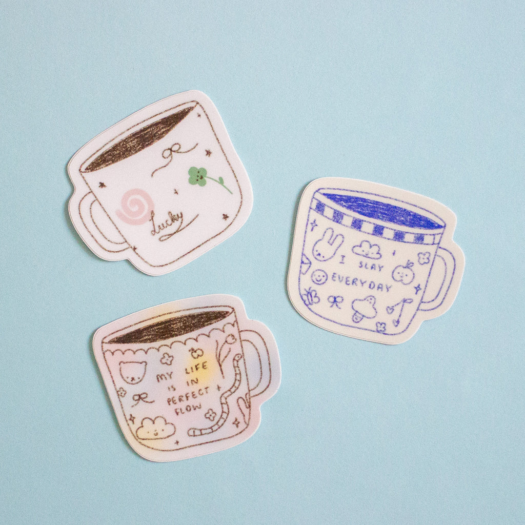 Three cute illustrated coffee mugs with pastel designs and text, arranged on a light blue background.