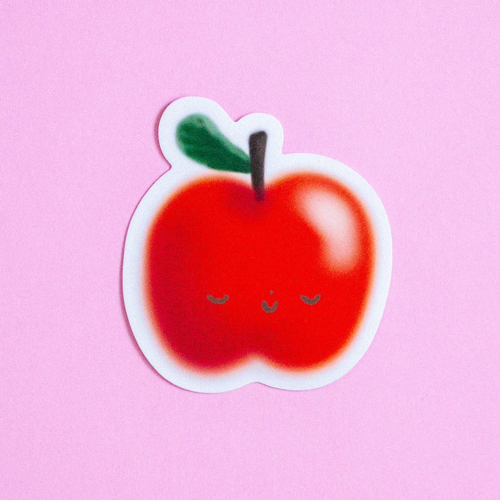 A cute die-cut sticker of a smiling red apple with a green leaf and closed eyes, shown on a solid pink background.