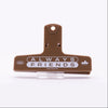 A brown plastic binder clip with black printed text reading 'ALWAYS FRIENDS' and '2025' on the front, displayed on a clear stand against a white background.