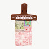 A brown plastic binder clip with black printed text reading 'ALWAYS FRIENDS' and '2025' on the front clipping a few sheets of paper, displayed against a white background.