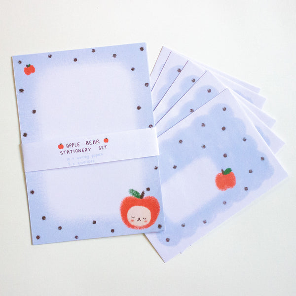 A stationery set featuring light blue paper sheets with dark polka dots, a small red apple illustration, and a white paper band reading 'APPLE BEAR STATIONERY SET'.