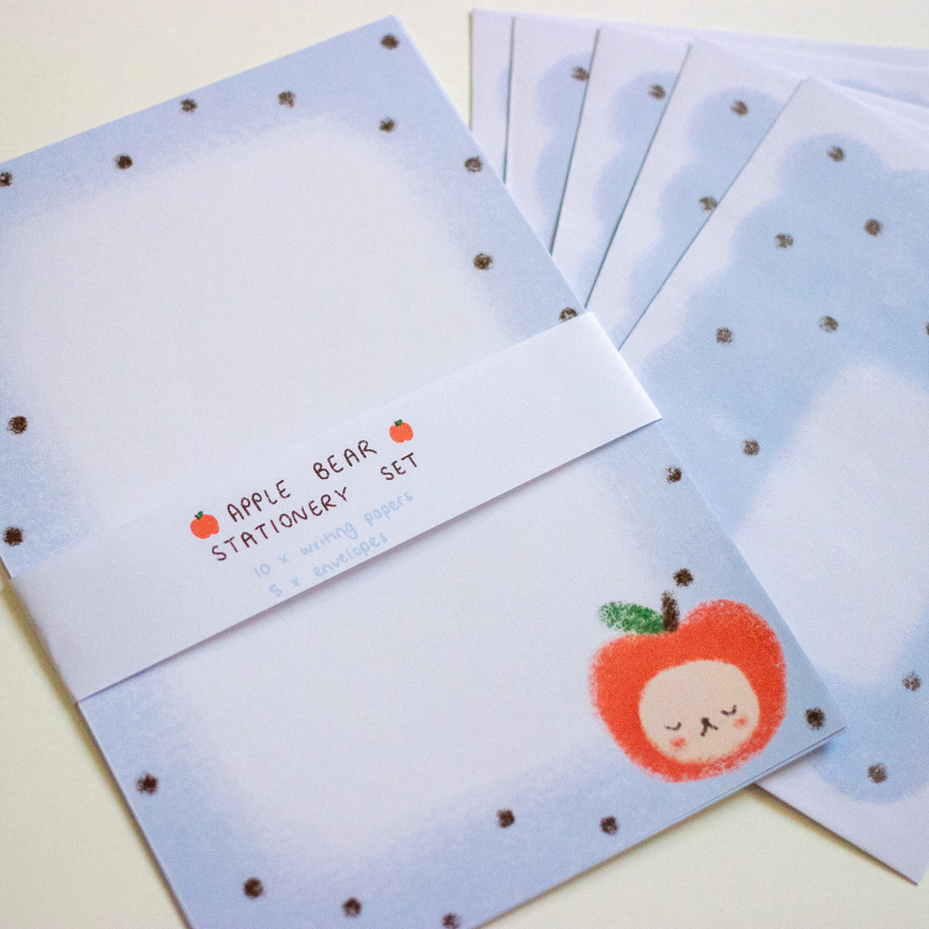 A set of stationery notepads and envelopes from Apple Bear, featuring a light blue watercolor design with dark brown polka dots, a white paper band, and a cute sleeping red apple character.