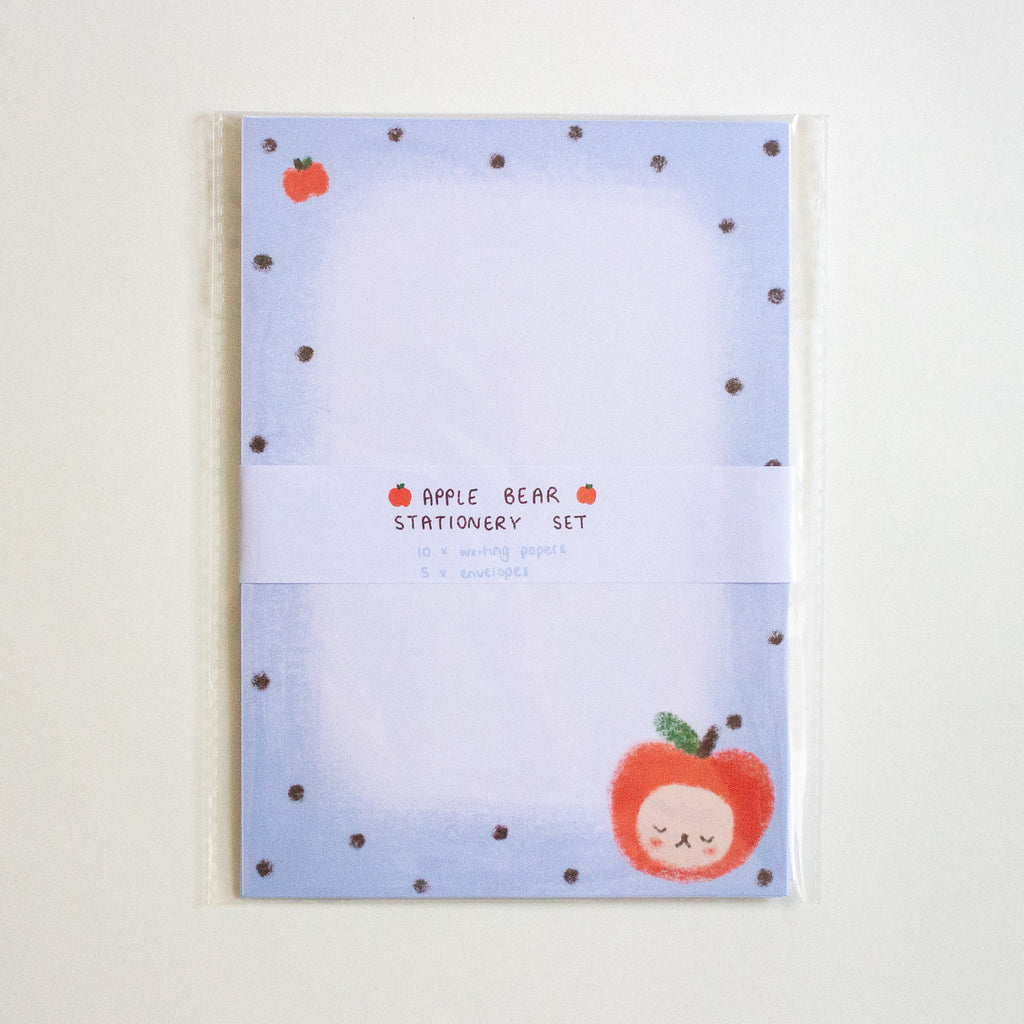 An Apple Bear stationery set in clear plastic packaging, featuring a light blue notepad with dark black polka dots, a cute red apple character, and a white paper band labeled 'APPLE BEAR STATIONERY SET'.
