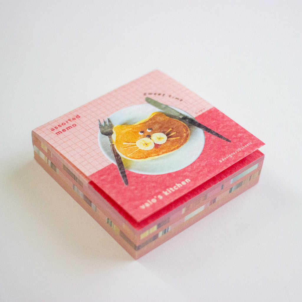 A stack of assorted memo pads with a pink and red grid pattern, featuring a cute illustration of a cat face on a slice of toast with a knife and fork. 