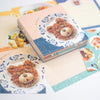 A stack of decorative paper memo sheets featuring cute food illustrations, including a bear-shaped pastry on a plate, arranged on a light surface.