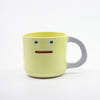 Yellow ceramic mug with a face design on a white background
