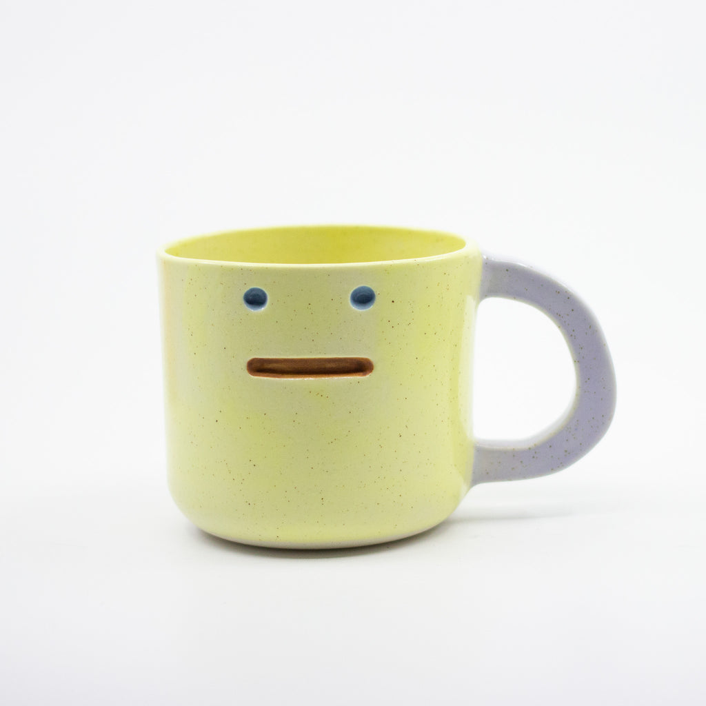 Yellow ceramic mug with a face design on a white background
