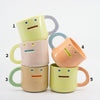 Five colorful mugs with face designs stacked on a white background