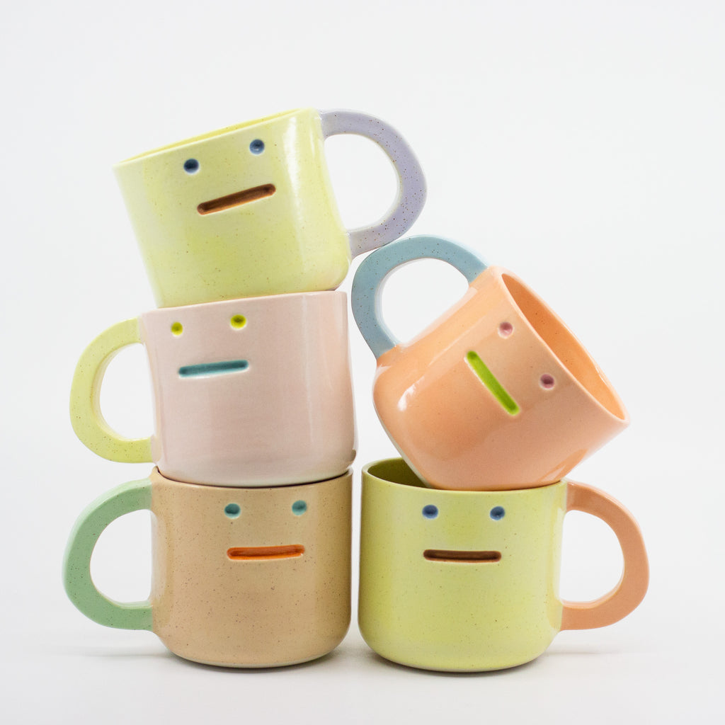 Set of colorful ceramic mugs with face designs on a white background