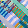 A close-up of a multicolour striped and checkered textile bath mat featuring textured terry cloth and woven striped patterns in blue, green, orange, pink, and purple.
