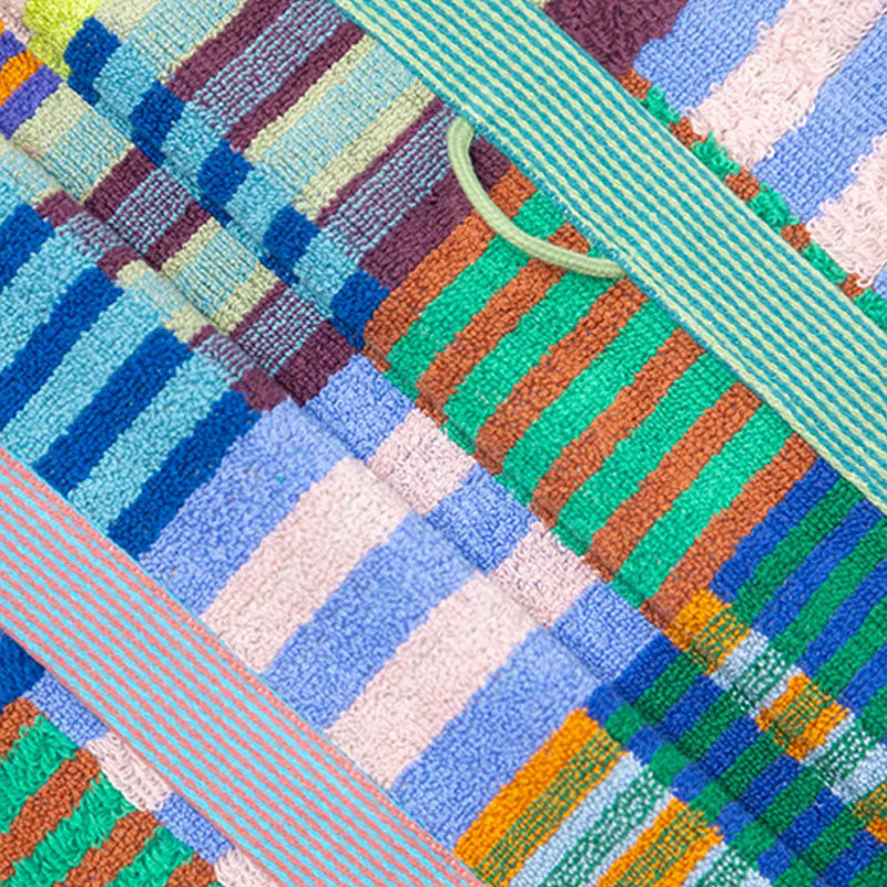 A close-up of a multicolour striped and checkered textile bath mat featuring textured terry cloth and woven striped patterns in blue, green, orange, pink, and purple.